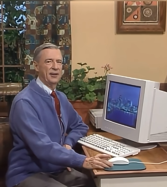 Mr. Rogers sitting beside a desktop computer.